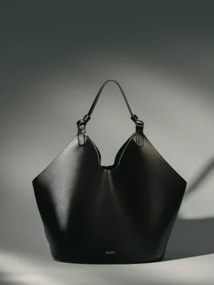 Black textured leather Khaite Lotus tote handbag displayed against a neutral gradient studio background with soft directional shadow.