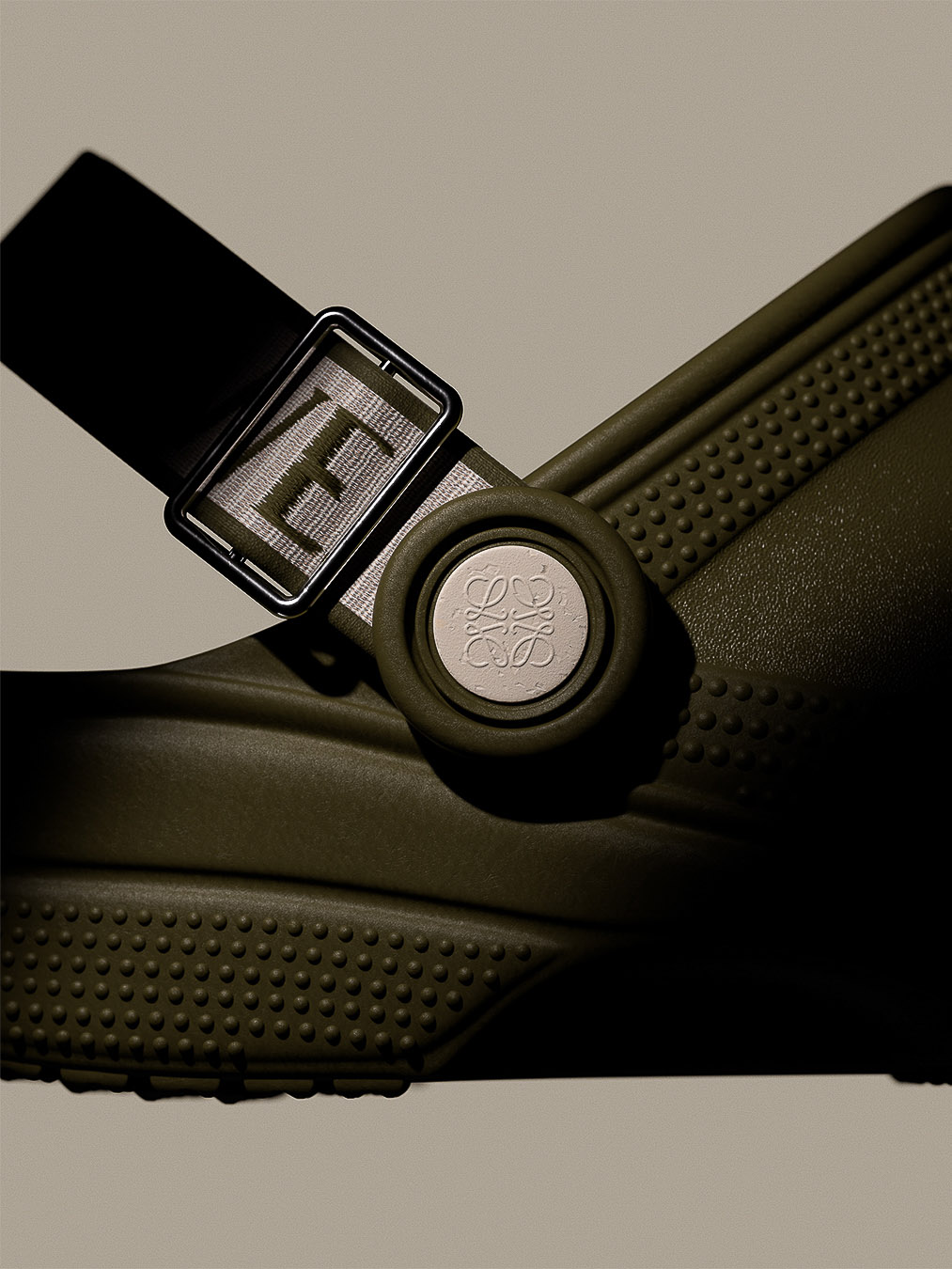 Olive green Crocs sandal with a black strap featuring the Loewe brand name and logo, studio shot against a neutral background.
