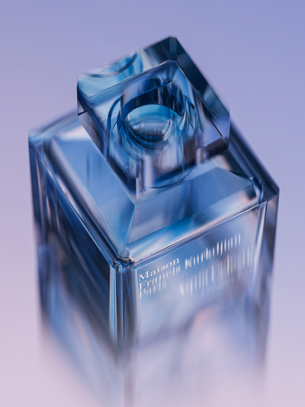 Close-up product shot of a square perfume bottle with a geometric cap, reflecting light and color against a lilac and blue background.