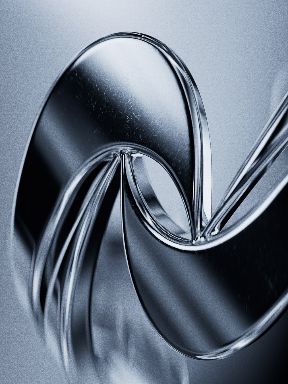Abstract macro photograph of reflective, curved metal ribbons on a soft gray background with studio lighting.