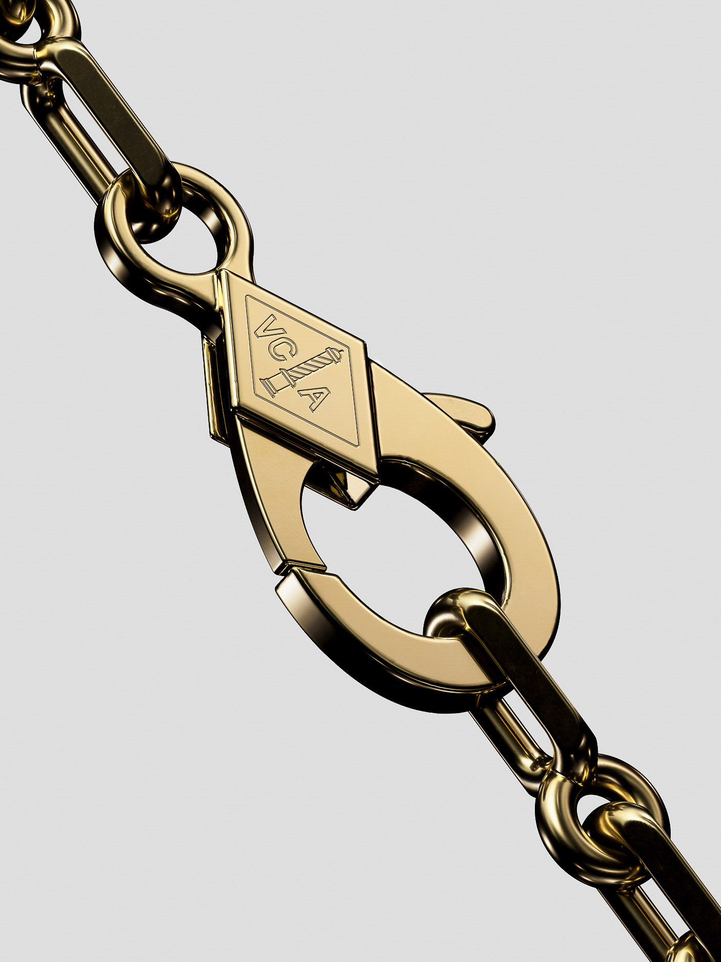 Close-up of a gold chain necklace with a lobster clasp and a diamond-shaped logo, set against a grey backdrop.