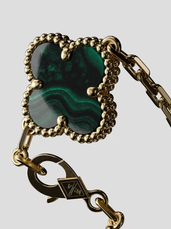 Close-up of gold chain-link bracelet with malachite clover pendant featuring intricate detail, against a neutral background. Studio lighting.