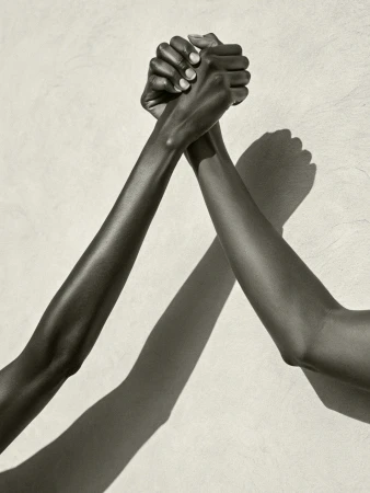 Close-up studio shot of two Black women's arms interlocked in a sign of unity, strength, and connection against a neutral background.