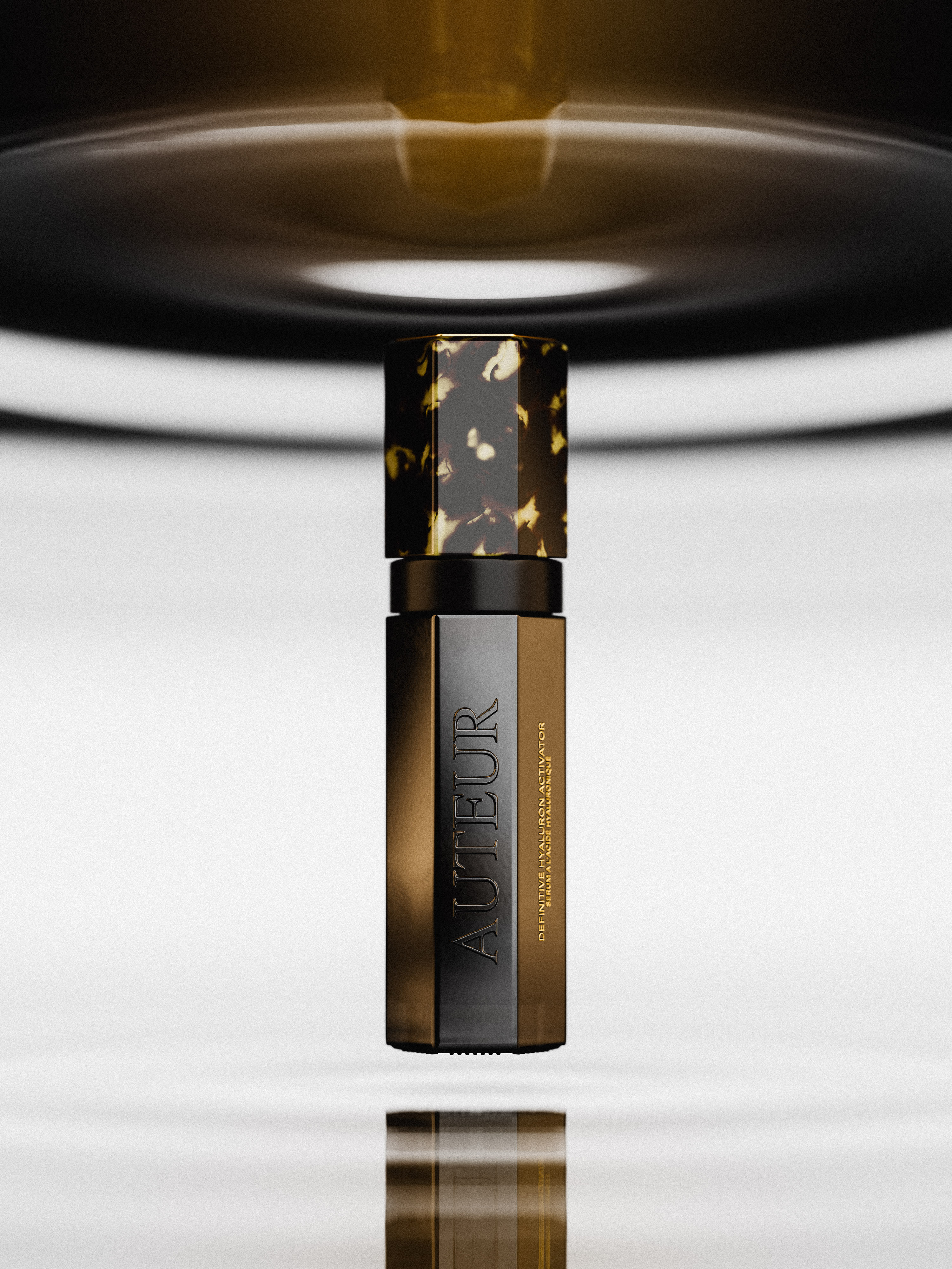 Product shot of gold-toned Autuer skincare serum bottle with marbled cap, showcasing minimalist design and reflective surface against a white background.