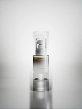 Elegant product shot of a clear and white cosmetic serum bottle with pump on a reflective surface against a gradient white background.