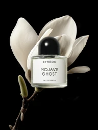 Byredo Mojave Ghost perfume bottle resting on a white flower stem against a solid black background.