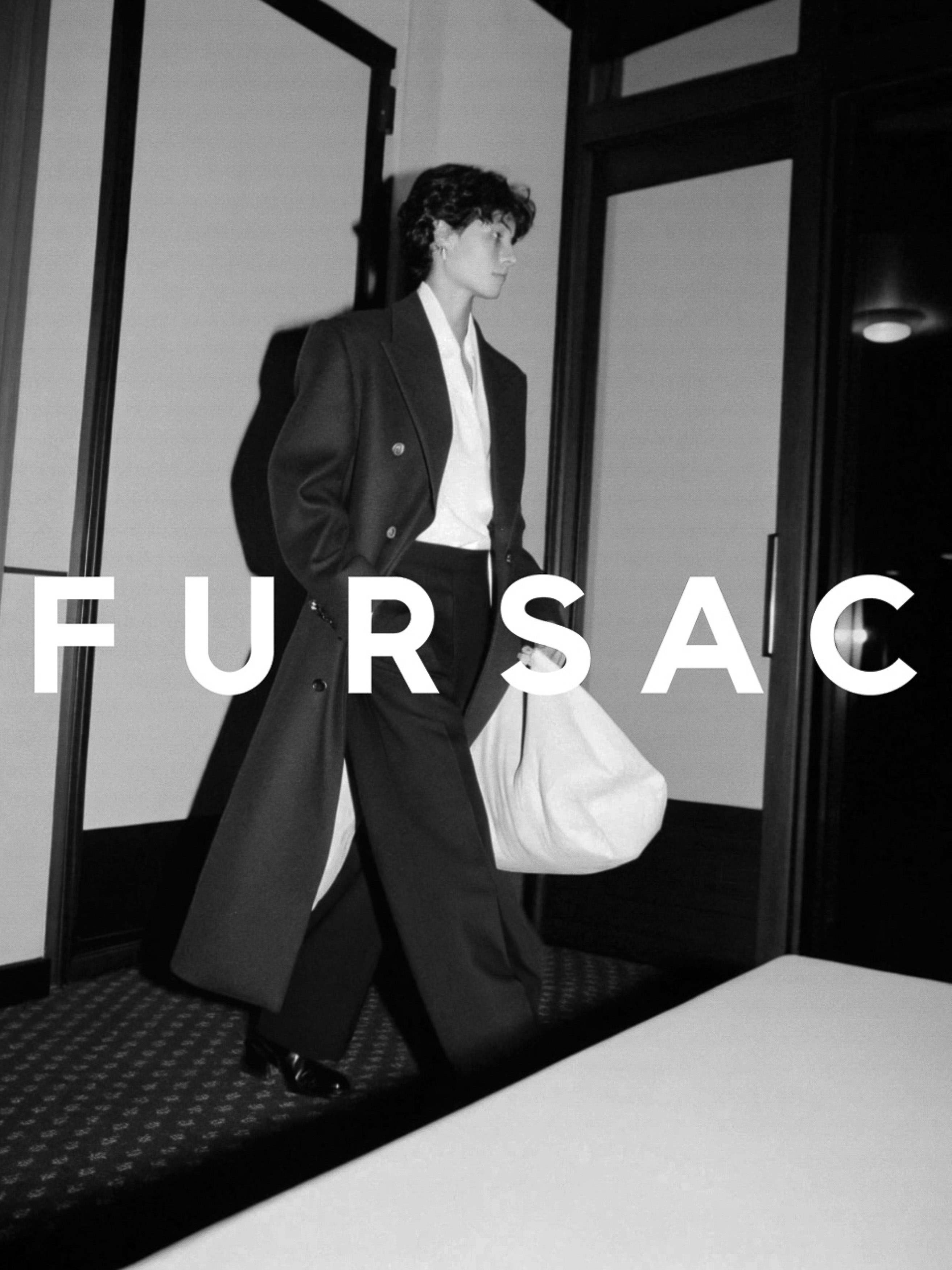 Monochrome fashion shot of a person in a coat and wide-leg pants carrying a white bag, walking on patterned carpet, featuring the Fursac logo.