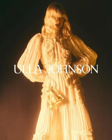 Fashion shot of a female model wearing an off-white Ulla Johnson gown in a studio setting, holding a small golden purse.