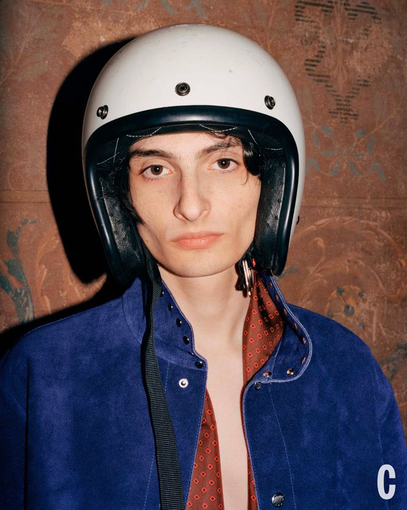 Portrait of a young adult wearing a white helmet, blue collared shirt, and a red patterned scarf in an indoor setting.