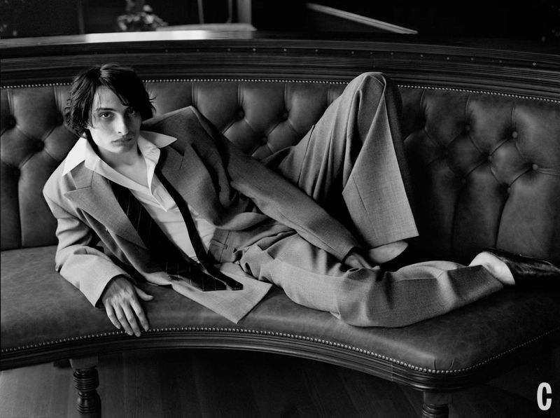 Black and white portrait of a young man in a suit reclining on a tufted leather couch, fashion photography, dark and moody aesthetic.
