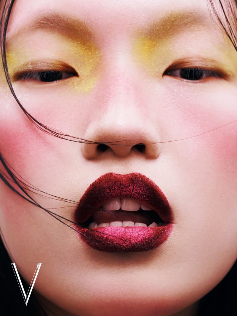 Close-up fashion beauty portrait of a young Asian woman with colorful makeup, dark lipstick, and fair skin in a photo studio.