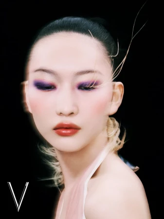 Close-up portrait of a woman with dark hair and dramatic purple eyeshadow, set against a stark black background with the letter V.