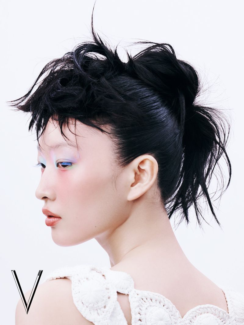 Profile view of a Black-haired Asian woman with bold makeup and a white crocheted top, set against a bright white background in a beauty shot.