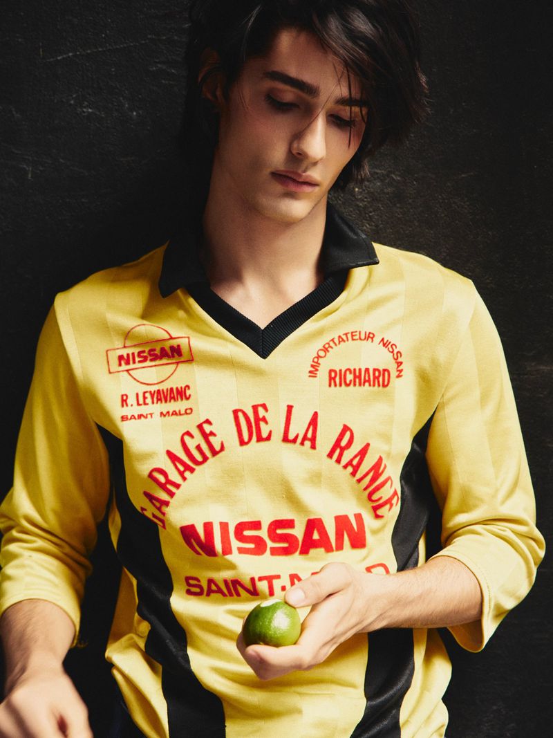 Portrait of a young adult male wearing a yellow jersey with black accents, holding a lime against a dark, textured background.