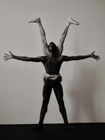Two dancers in a black and white photo, one African American man supporting a Caucasian dancer in pointe shoes with arms outstretched.
