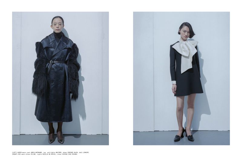 Two Asian women in high fashion: one in a black coat with fur sleeves, the other in a black dress with a large white bow, in studio.