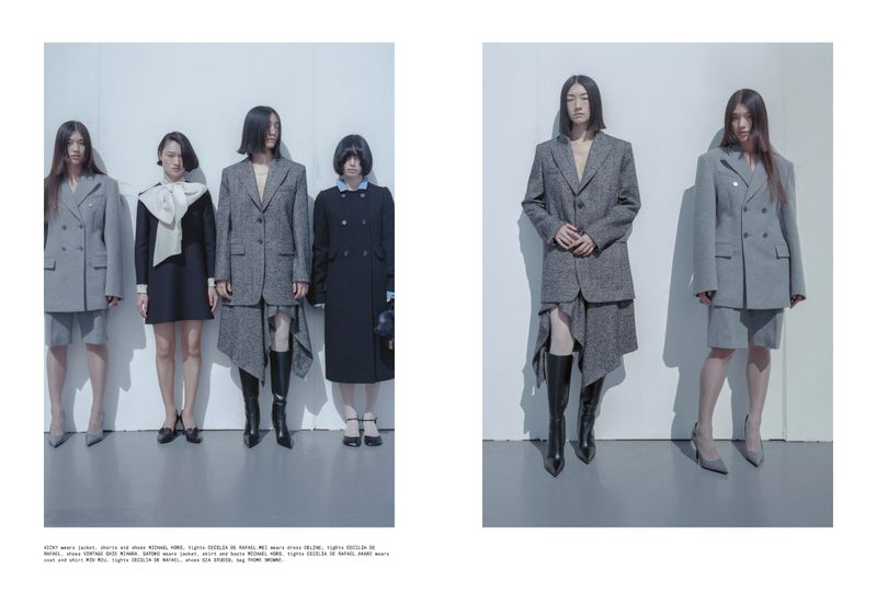 Fashion editorial shot of five women in diverse suit and dress styles, arranged against a minimalist white wall in a studio setting.