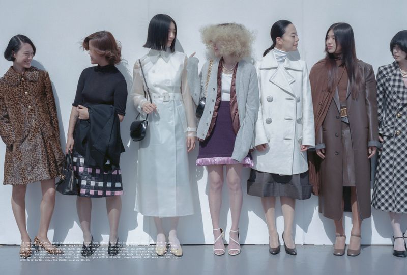 Seven Asian women stand in a row against a white background, showcasing an array of vintage-inspired dresses, coats, and heels in a fashion editorial.