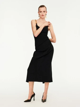 Elegant woman in a black dress and heels poses against a white backdrop, showcasing fashion and style with chic accessories and poise.