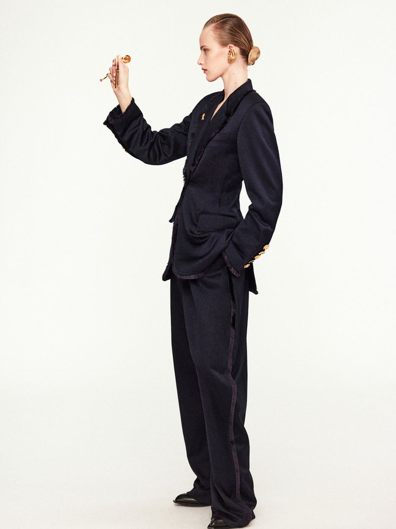 A model in a blue suit poses in a studio, looking at a pen. The image features fashion, a studio setting, and neutral colors.