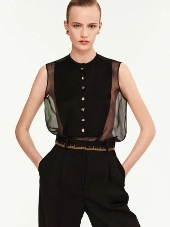 Fashion portrait of a fair-skinned woman with blonde hair wearing a black sleeveless top and trousers against a white backdrop.