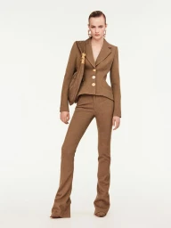 Model wearing a brown tailored blazer, trousers, and shoulder bag against a plain white background for Schiaparelli F/W25 lookbook.