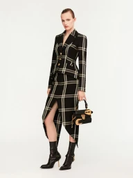 Model wearing a black and white plaid suit jacket and skirt holding a black handbag against a plain white background