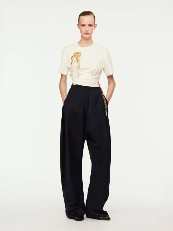 Lauren Huyskens wearing an off-white draped top and black wide-leg trousers against a white studio background.