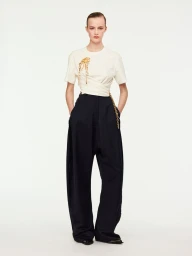 Lauren Huyskens wearing an off-white draped top and black wide-leg trousers against a white studio background.