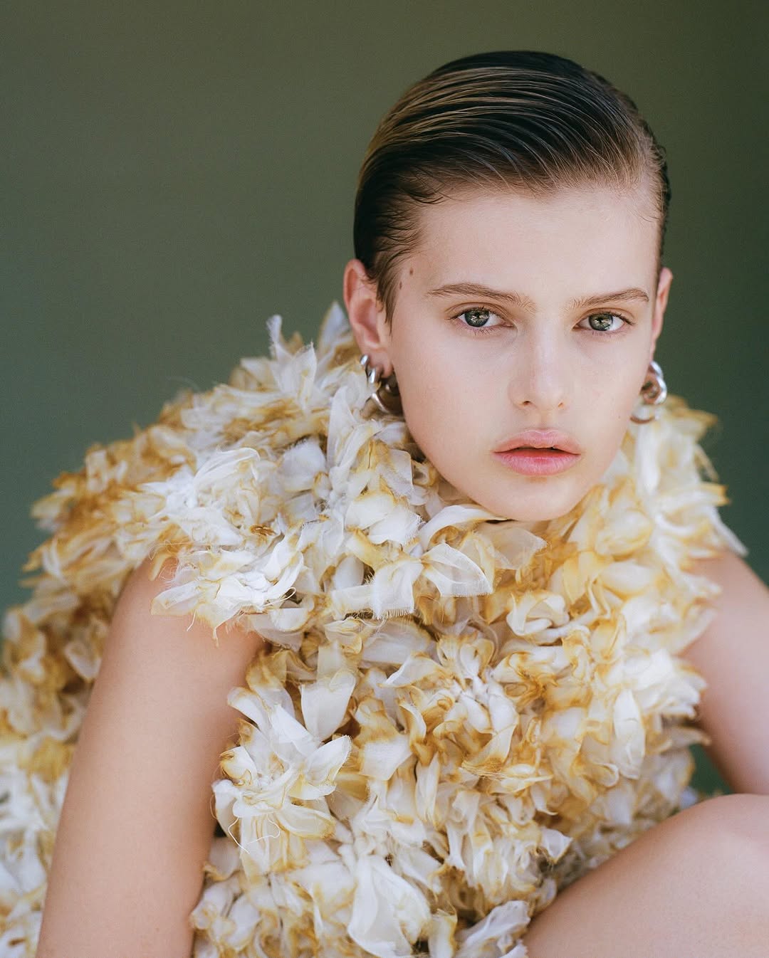 Young woman poses in a close-up studio shot with a floral ruffled garment, showcasing a beauty and fashion aesthetic.