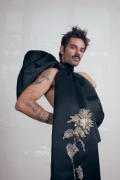 Man wearing a black structured haute couture top featuring a large embroidered flower applique against a seamless background