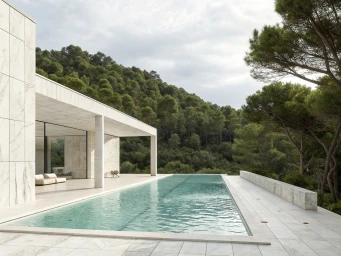 Modern minimalist villa terrace featuring a rectangular lap pool and white stone deck overlooking a lush pine forest.