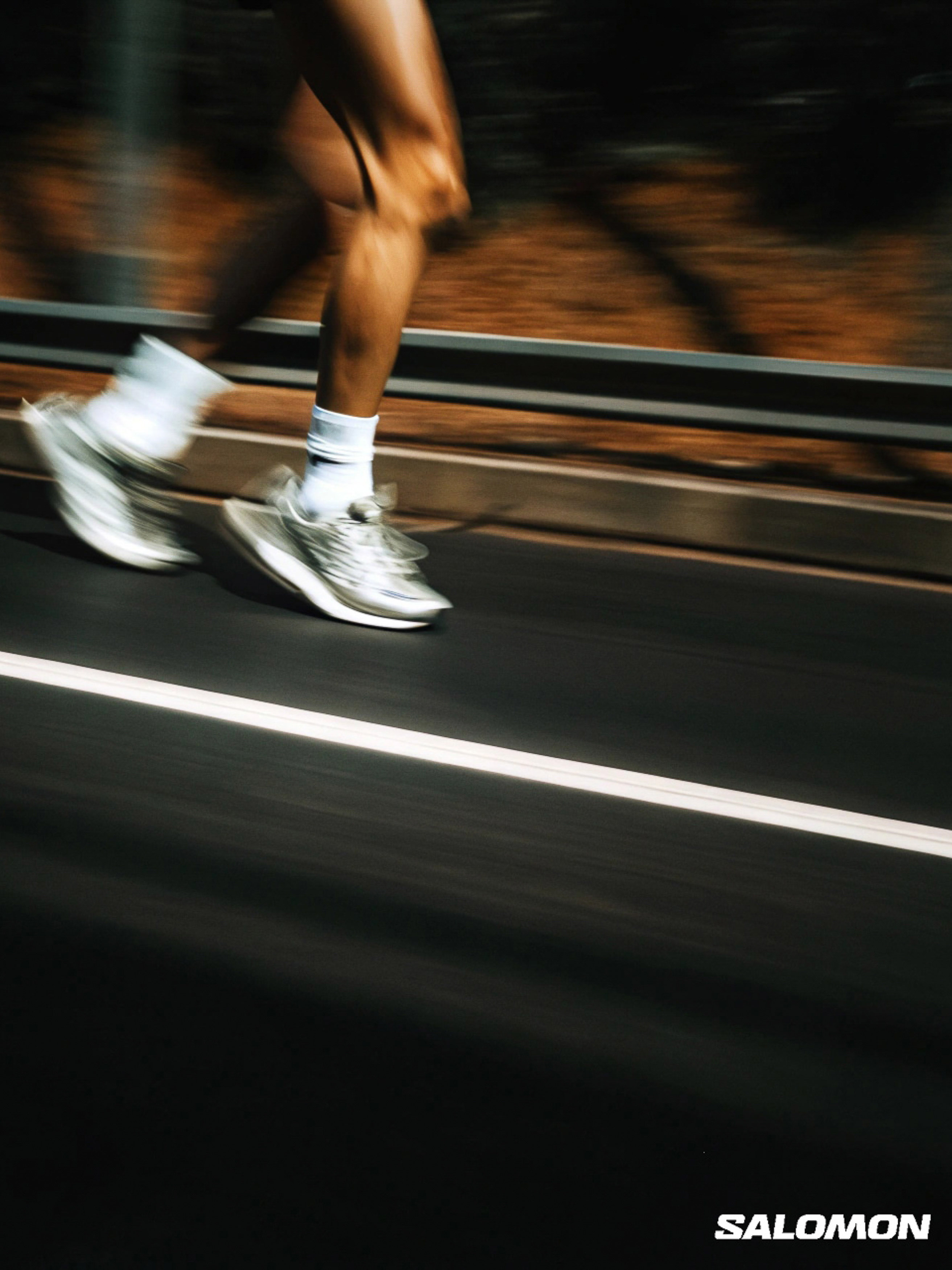 A person running on a road with motion blur, wearing running shoes and socks, with the Salomon logo visible at the bottom.