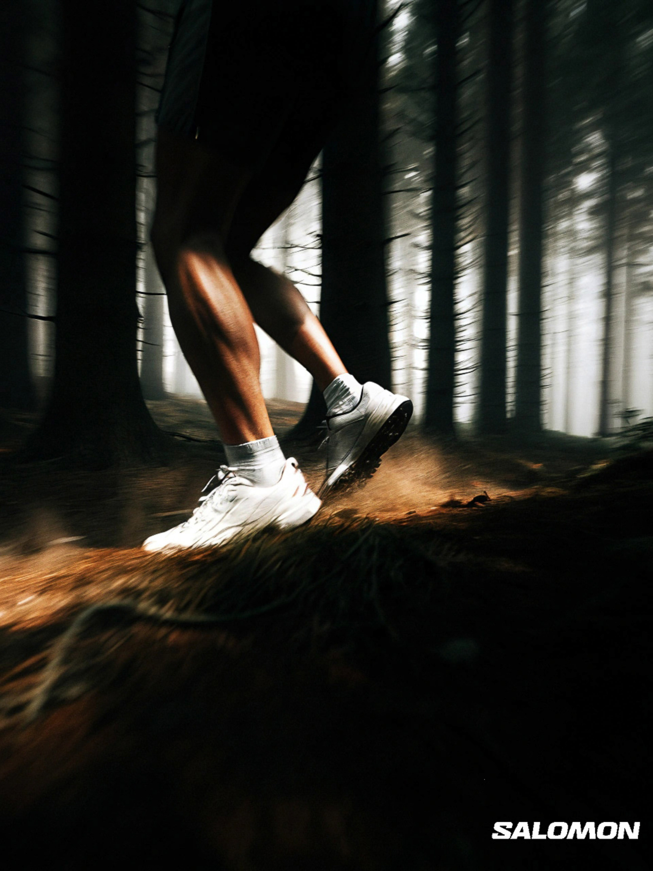 Low angle of a runner's legs and feet in motion on a dirt path surrounded by tall trees in a forest, showcasing athletic footwear.