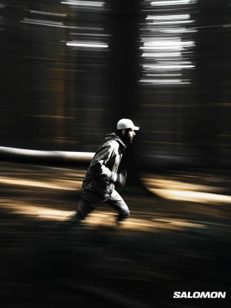 Adult male in sportswear runs through a forest with a motion blur effect, captured in a vertical, outdoor shot with diffused lighting.