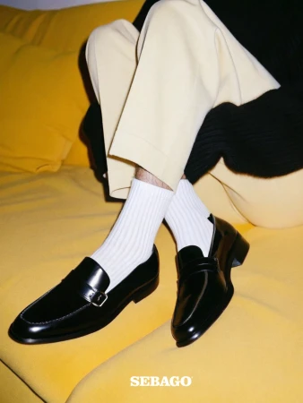 Close-up of two black leather Sebago loafers with white socks on a yellow sofa. Fashion product shot with indoor lighting.