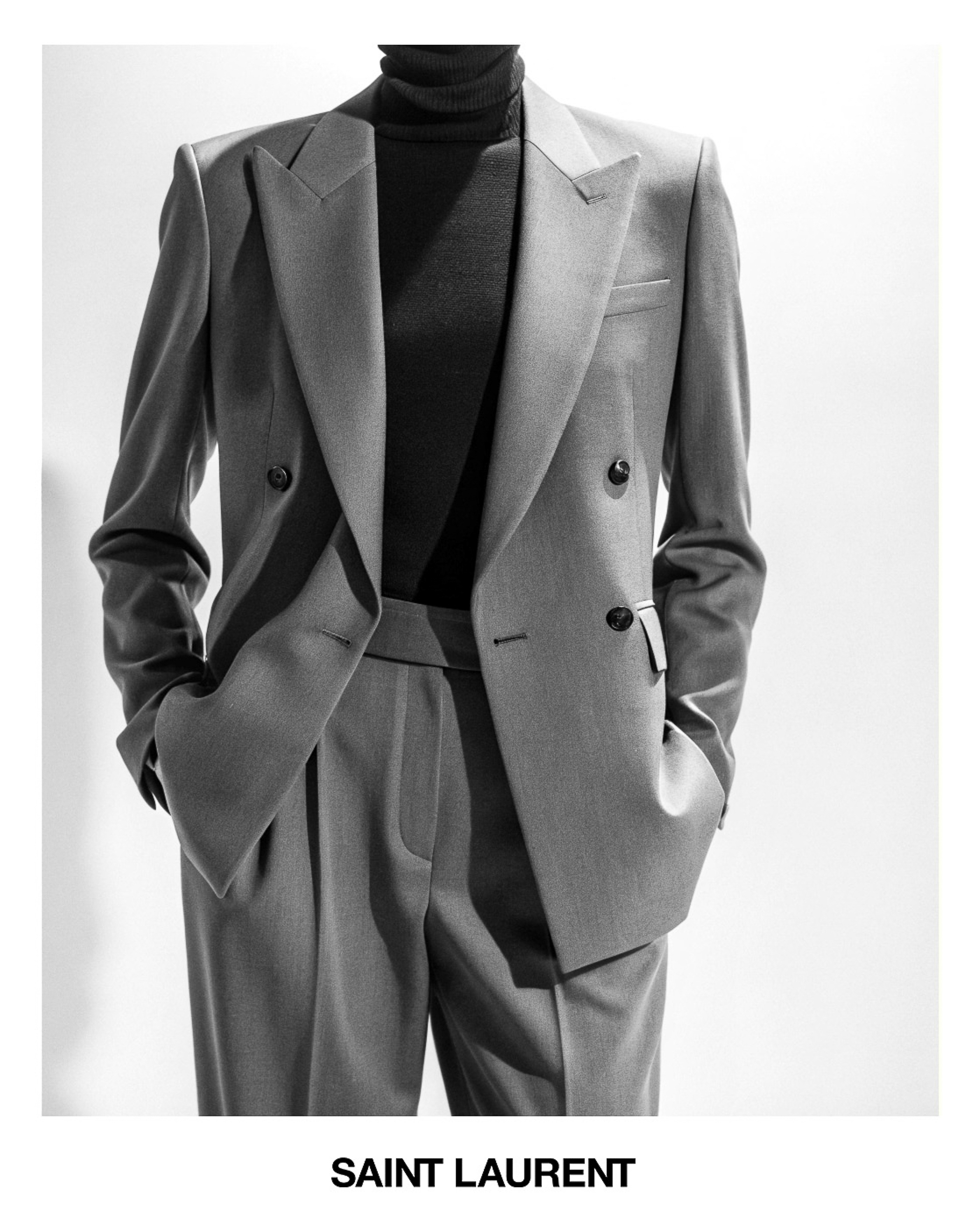 Black and white fashion shot of a grey tailored suit with a black turtleneck, in front of a white background. Saint Laurent logo visible.