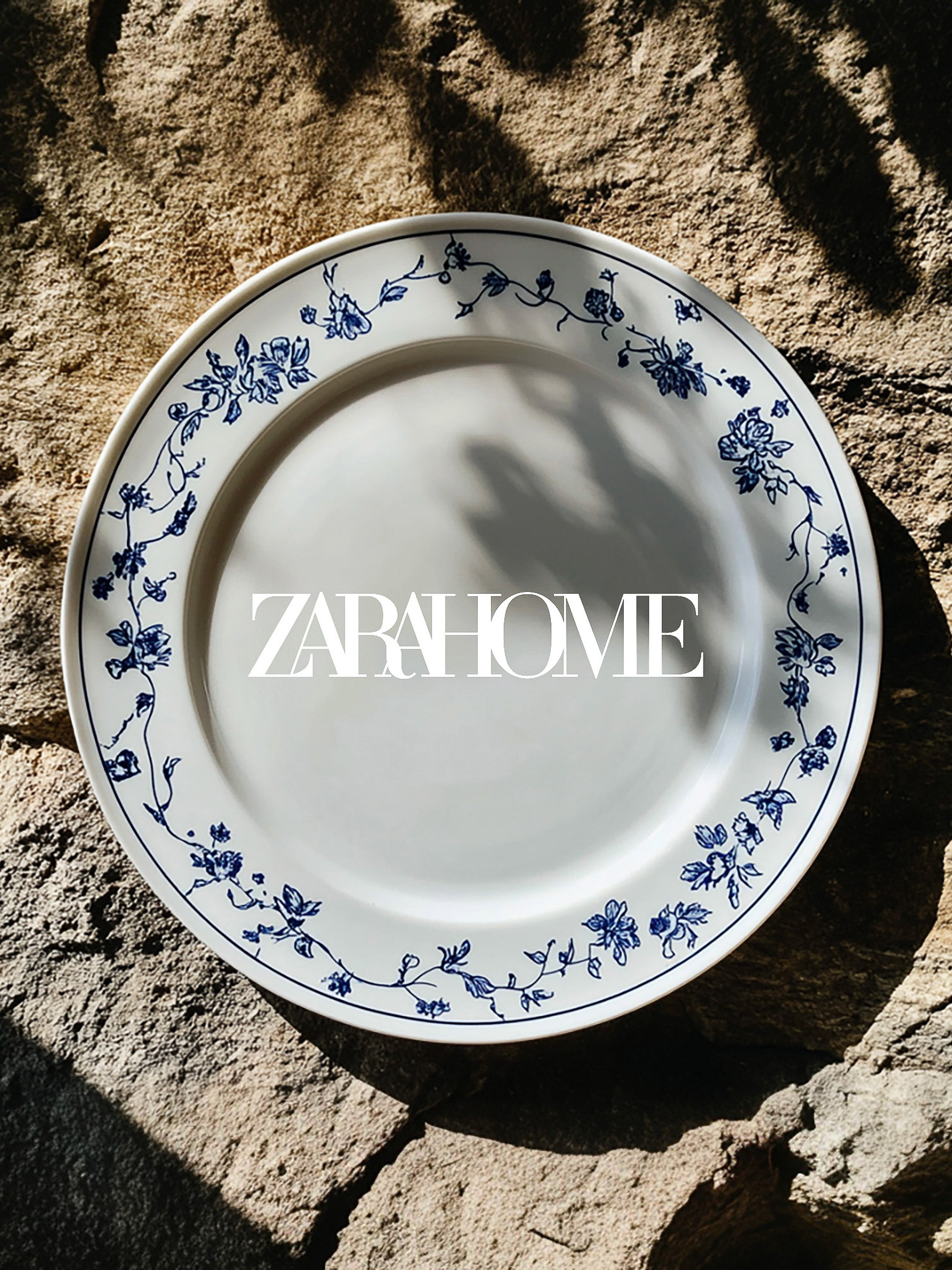 Overhead shot of Zara Home plate with blue floral pattern on stone background, casting shadows on the surface, high angle.