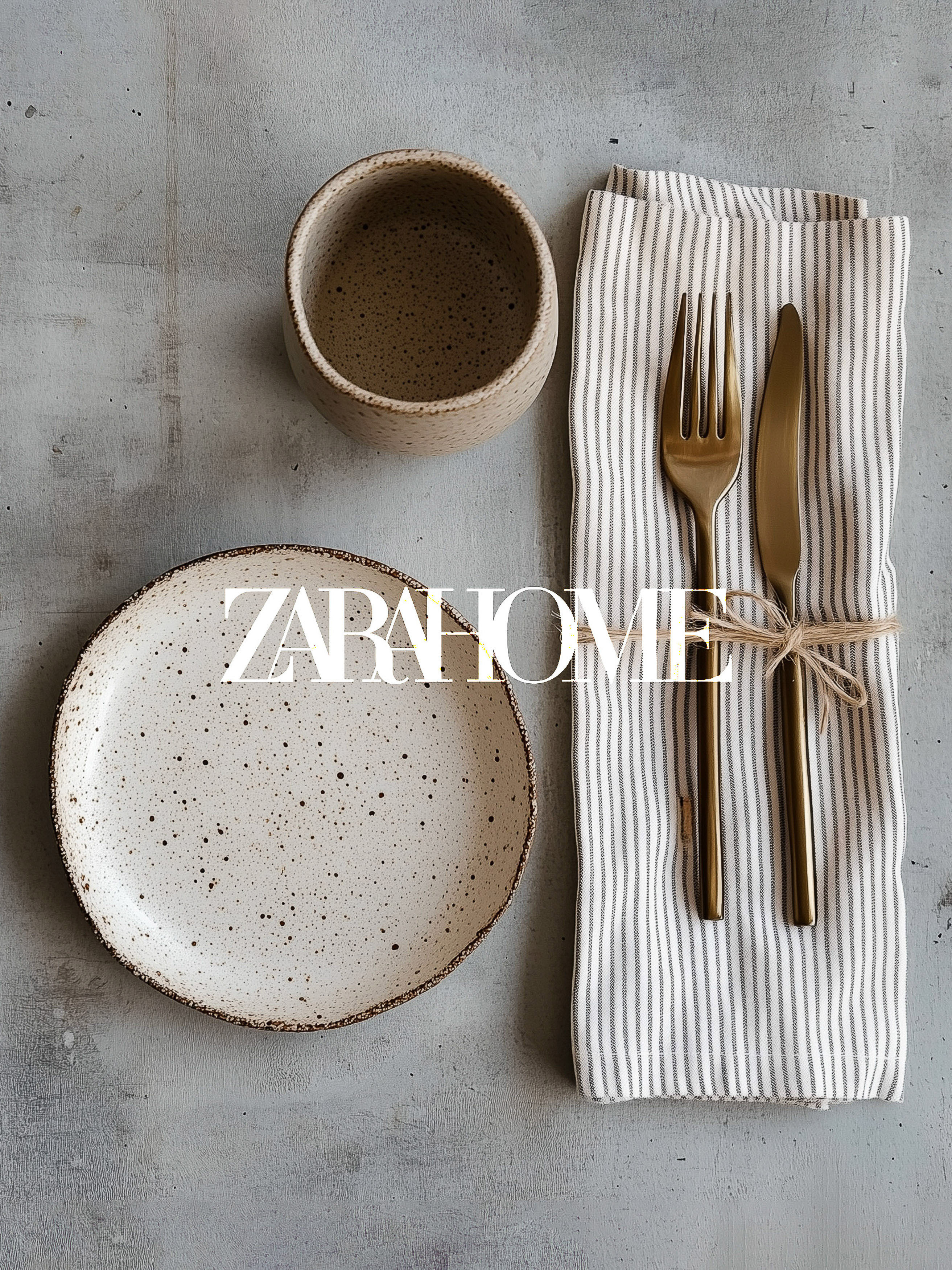 Overhead shot of a place setting with a speckled plate, mug, gold flatware, and striped linen napkin on a neutral gray surface.