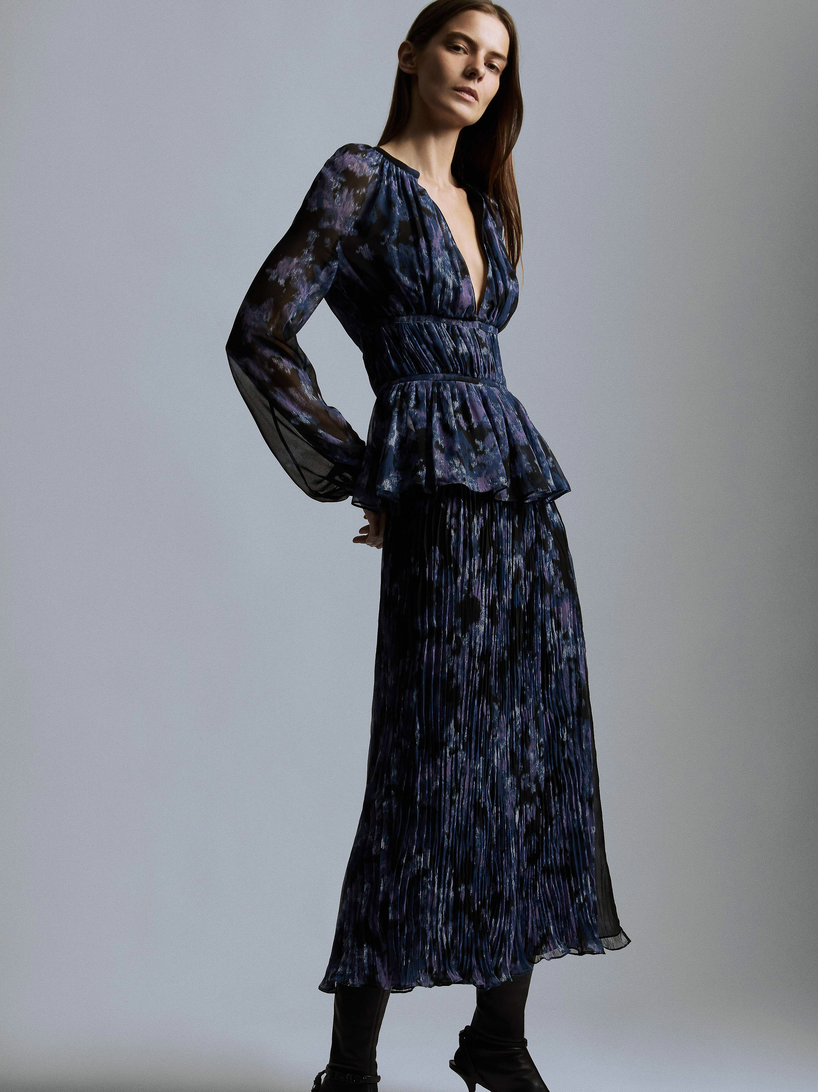 Model wearing a navy blue printed long-sleeve peplum top and pleated midi skirt against a neutral grey studio background.
