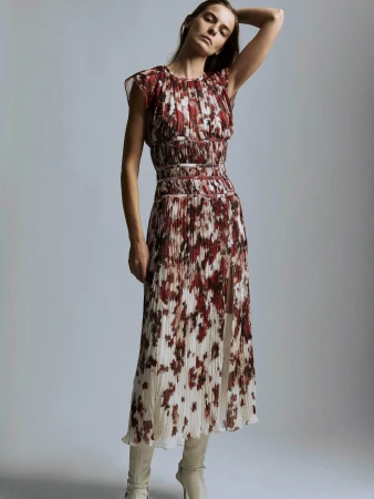 Model in a burgundy and white patterned pleated midi dress and cream knee-high boots posing against a grey studio backdrop.
