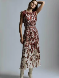 Model in a burgundy and white patterned pleated midi dress and cream knee-high boots posing against a grey studio backdrop.