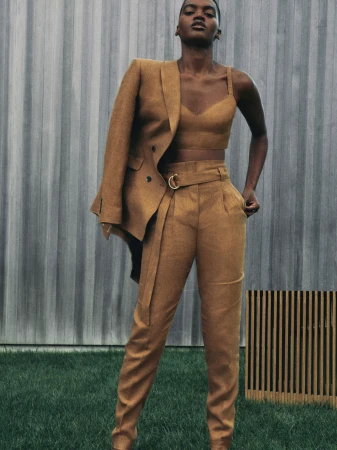 Professional studio shot of a Black woman in a brown linen suit, blazer draped over her shoulder, posing against an outdoor backdrop.