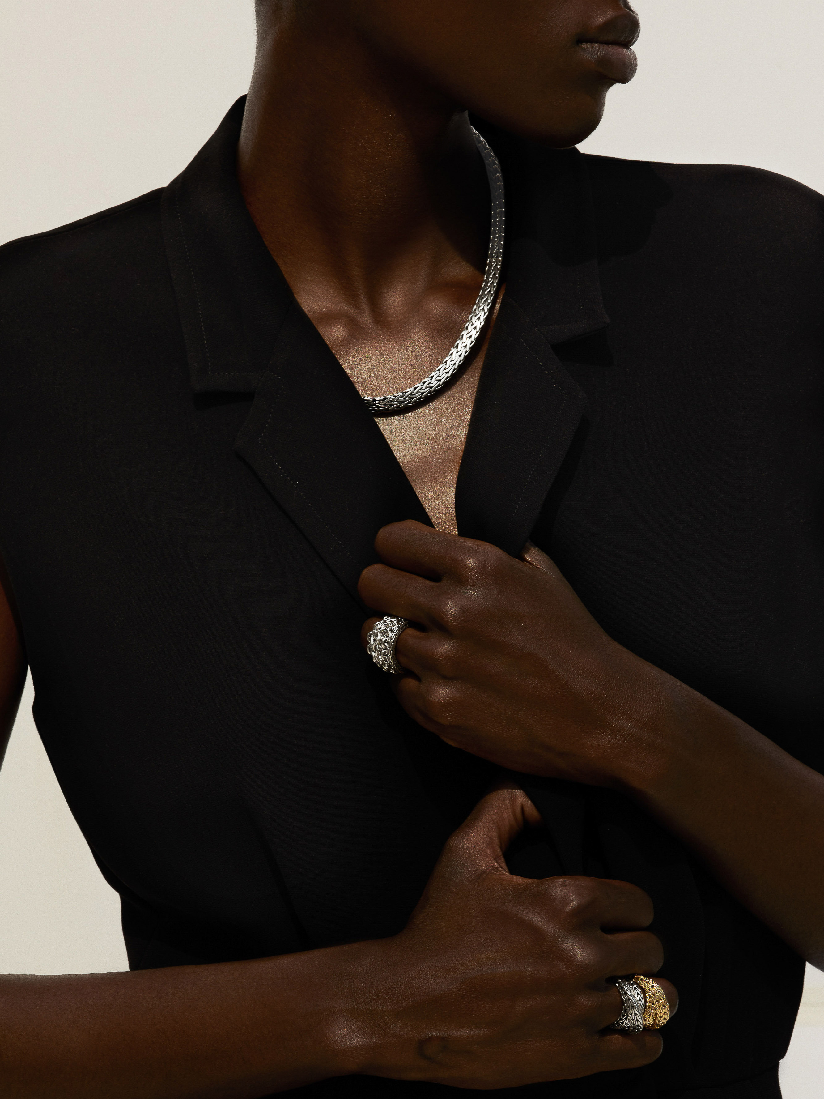 Close-up shot of a Black woman wearing a black vest, silver necklace, and decorative rings on her fingers against a neutral backdrop.