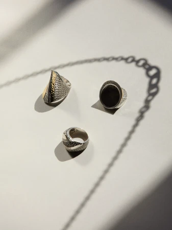 Three silver rings displayed on a white surface with a long shadow cast by a chain-like object, creating a play of light and shadow.