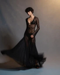 Model in a black sheer lace long-sleeved dress with motion blur on the skirt against a grey studio backdrop.