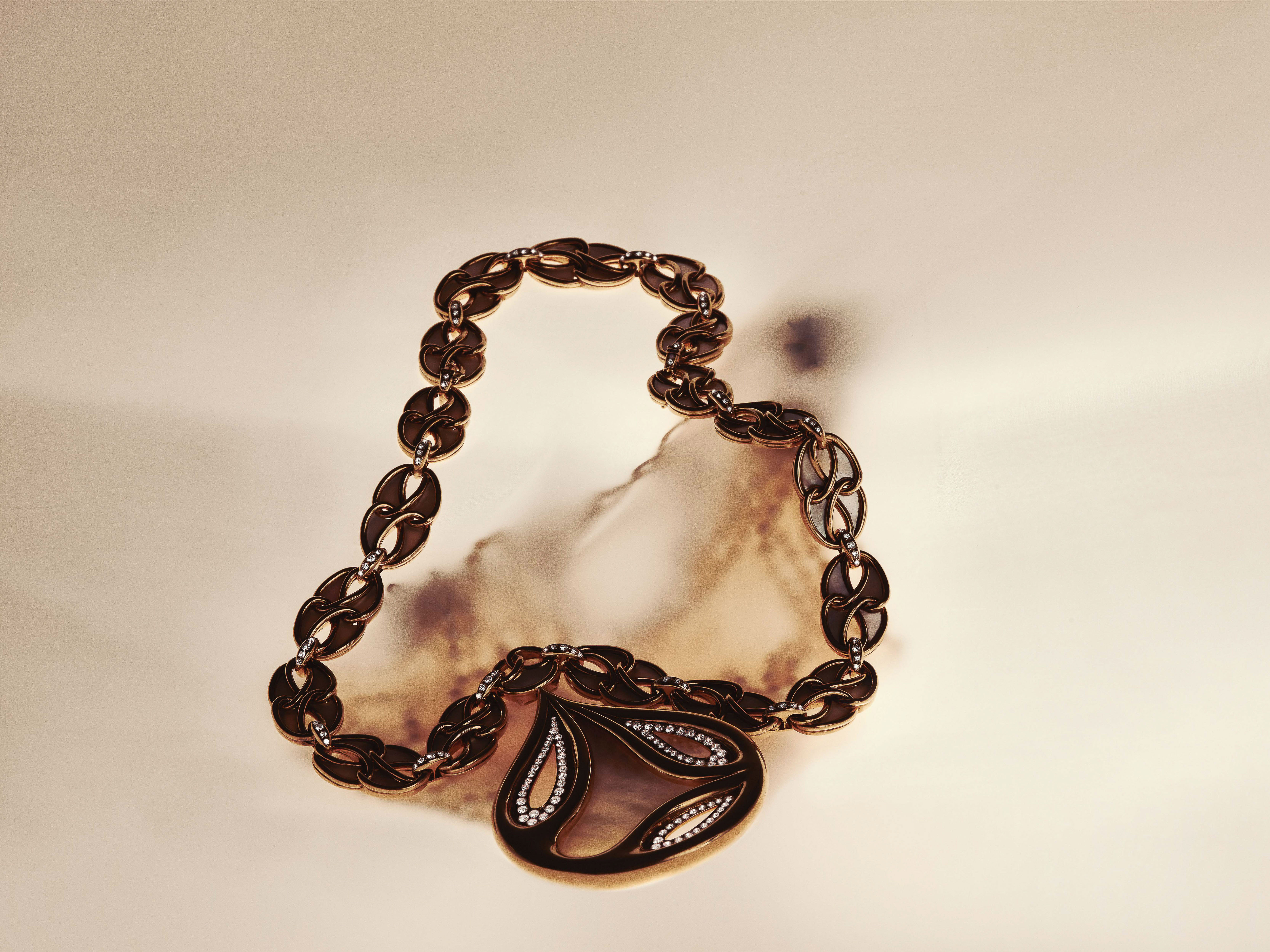 Gold and gemstone link necklace with a sculptural drop pendant placed on a warm neutral surface with soft shadows.