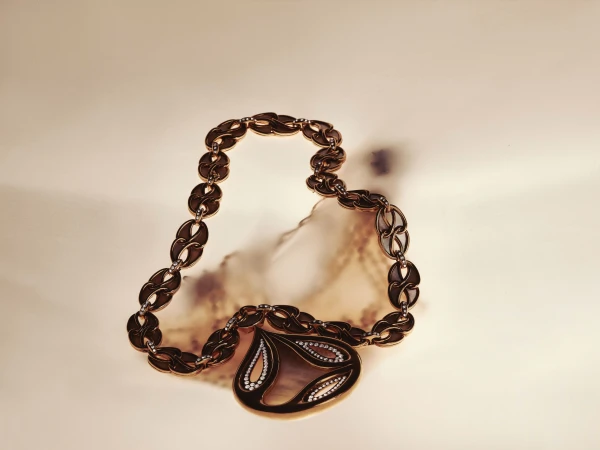 Gold and gemstone link necklace with a sculptural drop pendant placed on a warm neutral surface with soft shadows.