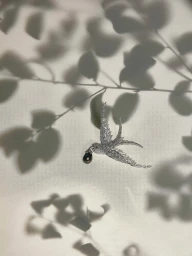 Diamond encrusted bird brooch carrying a black pearl droplet against a light surface with leaf shadows.