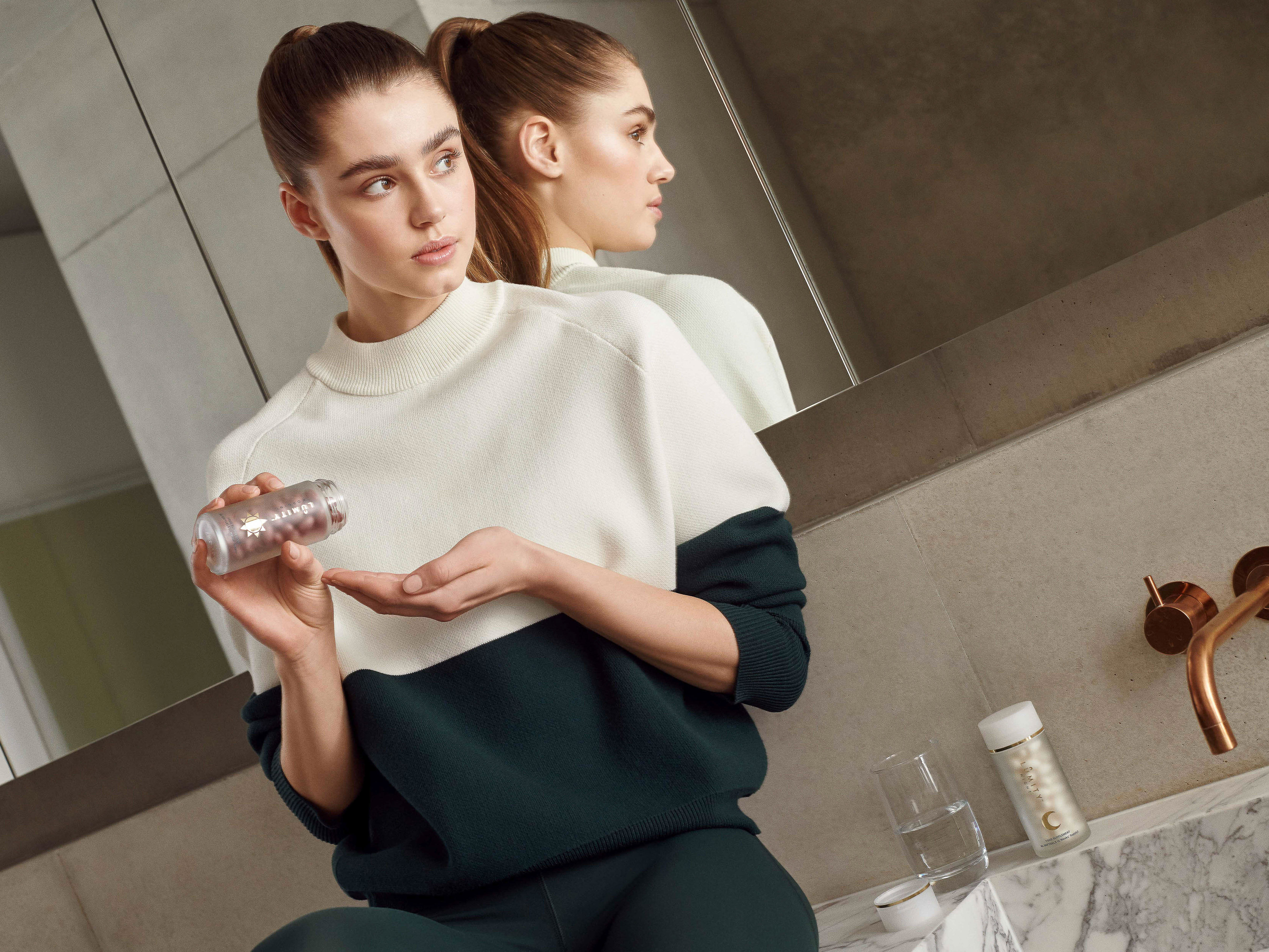 Indoor beauty shot features a young woman in sportswear, holding a pill bottle, with a reflective background and natural light.